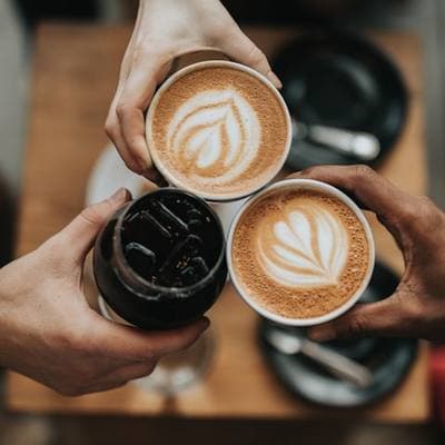 Two lattes with poured art, held over a table